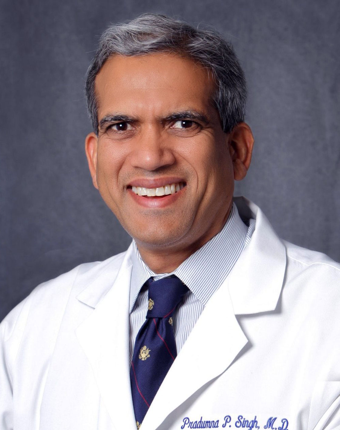 Man in white lab coat smiling, posing for portrait.