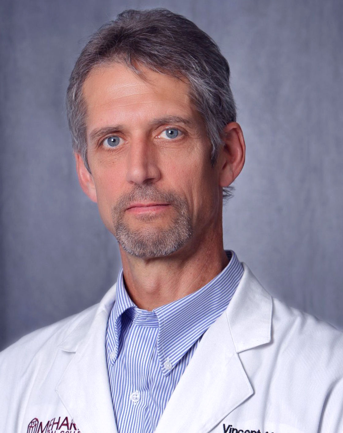 Man in white lab coat, smiling, posing for portrait.