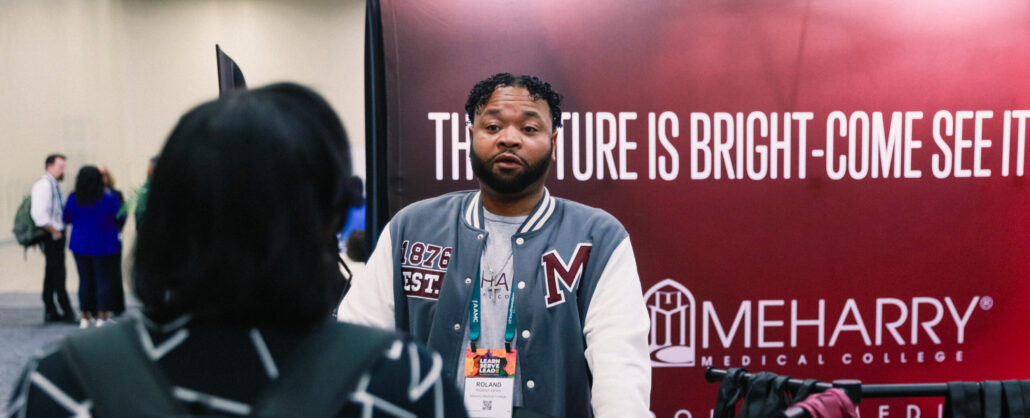 A man standing at a booth with promotional material in the background.