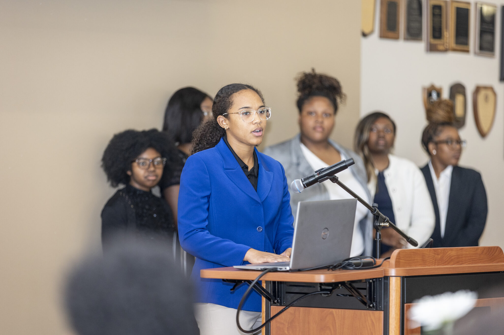 A young woman in a blue blazer giving a speech at a podium.
