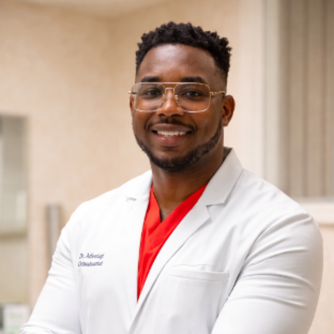 Man wearing glasses, red shirt, white coat, standing in a room.