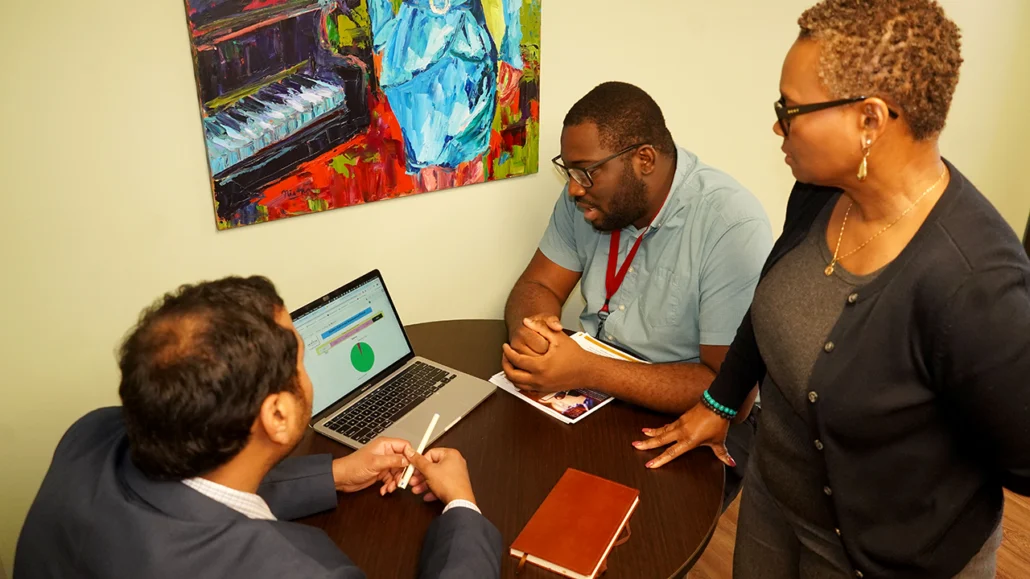 three staff examine data analysis on laptop