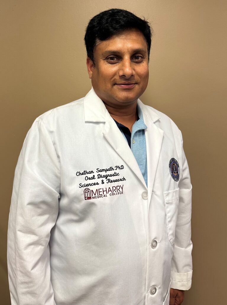 Man wearing white lab coat, standing against light background.